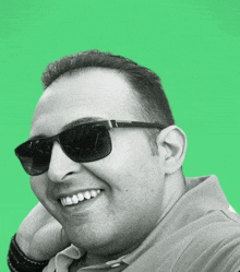 a man wearing sunglasses and a green shirt smiles for the camera