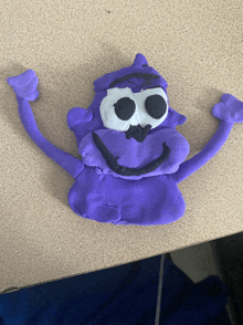 a purple stuffed animal with black eyes and arms