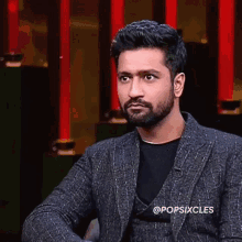 a man with a beard wearing a suit and a black shirt is sitting in front of a red wall .