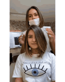 a woman wearing a white t-shirt with an eye on it is getting her hair cut by a hairdresser .