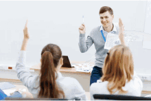 a man holds up a piece of paper in front of a group of students who are raising their hands