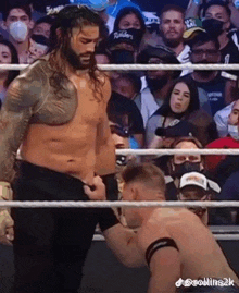 roman reigns is standing in the middle of a wrestling ring with a crowd watching him .