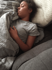 a woman is sleeping on a bed with a grey blanket