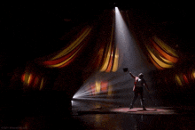 a man in a top hat stands on a stage in the spotlight