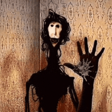 a scary doll is standing in a room with a hand reaching out towards it .