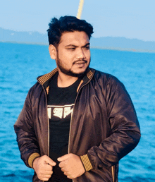 a man wearing a black shirt that says ' i love you ' on it is standing in front of a body of water