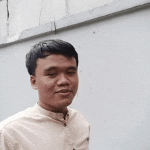 a young man in a tan shirt stands in front of a wall