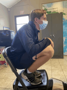 a man wearing a face mask squats in front of an exit sign