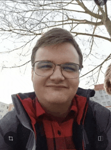 a man wearing glasses and a red plaid shirt is smiling