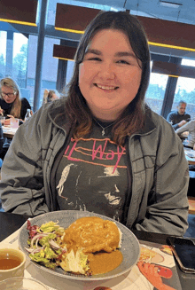 a woman wearing a t-shirt that says the way is smiling in front of a plate of food