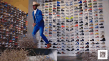 a man wearing a cowboy hat is standing in front of a wall of shoes with complex written on the bottom