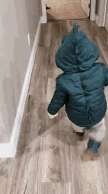 a little boy wearing a dinosaur jacket is walking down the hallway