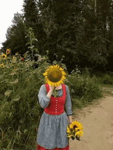 a woman in a red dress is holding a bouquet of sunflowers and covering her face with a sunflower .