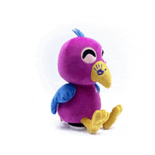 a purple stuffed bird with blue wings and a yellow beak is sitting on a white surface