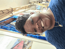 a woman in a blue sweater is smiling in front of a wall with a picture of a boat on it