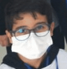 a young boy wearing a face mask and glasses is looking at the camera .