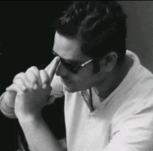 a man wearing sunglasses and a white shirt is praying with his hands together .