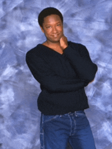 a man wearing a black sweater and blue jeans stands with his arms crossed