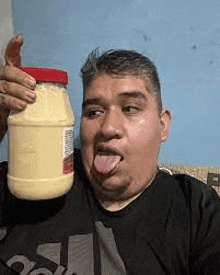 a man is sticking his tongue out and holding a jar of mayonnaise .