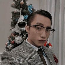 a man wearing glasses and a suit is standing in front of a christmas tree