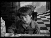 a black and white photo of a young boy sitting at a table with a box of donald duck milk .