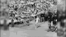 a black and white photo of a woman holding a torch in front of a crowd with the olympic rings in the background