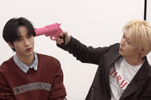 a man holding a pink gun over another man 's head who is wearing a shirt that says ' army '