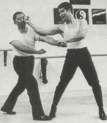 two men are practicing martial arts in front of a wall with a picture of a yin yang on it