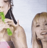 a woman is holding a green object in her mouth and another woman is holding a green object in her mouth .