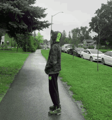 a person wearing a green hoodie stands on a path in the rain