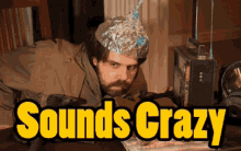 a man wearing a tin foil hat sits at a table with the words " sounds crazy " in yellow letters