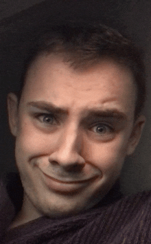 a close up of a man 's face with a purple shirt on