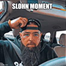 a man with a beard is sitting in the driver 's seat of a car with the caption " slohn moment "