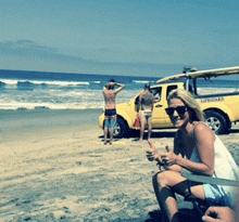 a woman sits on the beach next to a yellow truck that says lifeguard on the back