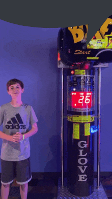 a boy wearing an adidas shirt is standing in front of a glove machine