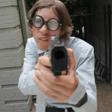 a man wearing glasses is pointing a gun towards the camera