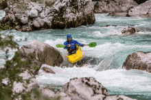 a man in a blue jacket is paddling a yellow kayak with a green paddle that says r on it