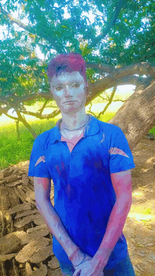 a man in a blue shirt is standing under a tree with his hands on his hips