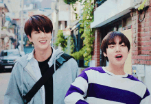 two young men are walking down a street and one of them is wearing a purple and white striped sweater