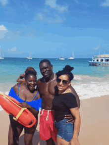 a man and two women pose for a picture on a beach with a boat in the background that says ' pirate ' on it