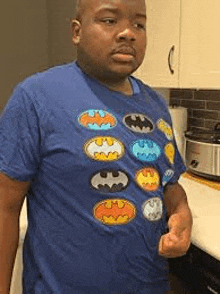 a man is wearing a blue batman t-shirt and standing in a kitchen .