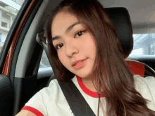 a young woman is sitting in a car wearing a seat belt and taking a selfie .