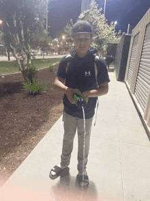 a boy wearing a under armour shirt is standing on a sidewalk at night