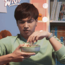 a man in a green shirt is eating a bowl of food with a sign in the background that says why