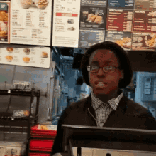 a man wearing glasses is standing in front of a counter with a menu behind him that says " snacks & desserts "