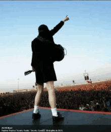 a man standing on a stage holding a guitar in front of a crowd with ac dc brasil written on the bottom