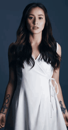 a woman in a white dress has a tattoo on her arm