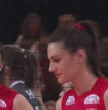 a woman in a red volleyball uniform is standing next to a volleyball net and smiling .