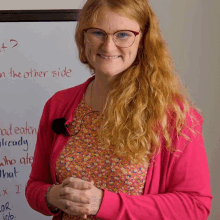 a woman in a pink sweater stands in front of a white board that says " what " on the other side