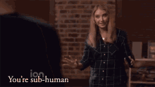 a woman is standing in front of a brick wall and saying you 're sub-human artificial unintelligence .